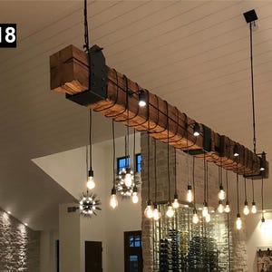 May include: A rustic, wooden beam chandelier with exposed Edison-style light bulbs hanging at varying lengths. The beam is supported by black metal brackets and wire. The fixture is suspended from the ceiling, providing ambient lighting.