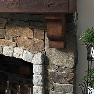 May include: A rustic stone fireplace with a wooden mantel and a decorative wooden corbel. The fireplace is surrounded by a variety of stonework, including granite and slate.