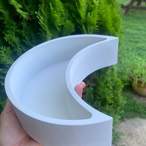 May include: White crescent moon shaped planter. The planter is made of a smooth, white material and has a rounded edge.