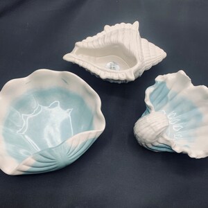 May include: Three ceramic seashell-shaped bowls. Two bowls are white with blue accents and one bowl is white with a blue interior.