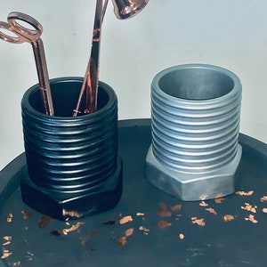 May include: Two decorative containers made to look like large nuts. The container on the left is black and the container on the right is silver. Both containers are sitting on a black surface with gold flecks.