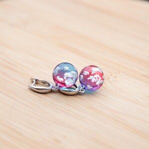 May include: A pair of silver hoop earrings with a pink and blue gradient resin sphere with white flecks, resembling clouds, hanging from each hoop.