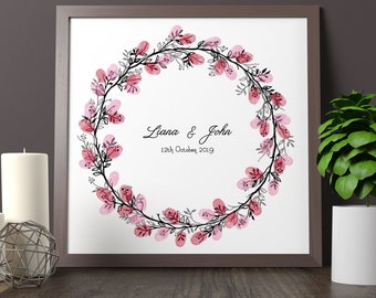 May include: A framed print with a watercolor wreath of pink flowers and black branches. The wreath is made up of fingerprints. The text "Liana & John 12th October 2019" is printed in black below the wreath.