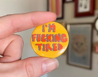 May include: A yellow button with the text "I'M FUCKING TIRED" in red and green letters.