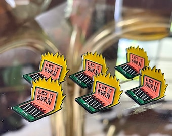 May include: Five enamel pins with a retro design. Each pin features a cartoon laptop with a flame coming out of the screen and the text "Let it Burn". The pins are yellow, red, green, and black.