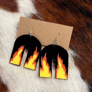 May include: A pair of black arch-shaped earrings with yellow and orange flames. The earrings are on a brown background.