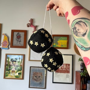 May include: Two black felt dice with white stars hanging from a white string. The dice are about 3 inches in diameter.