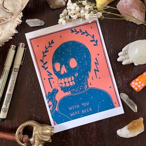 May include: A pink and blue illustration of a melting skull holding a bottle of beer. The text reads "Wish you were beer."