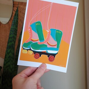 Puede incluir: Un par de patines de ruedas verdes y azules con ruedas rosas. Los patines tienen las palabras "Hell Yeah" escritas en ellos.