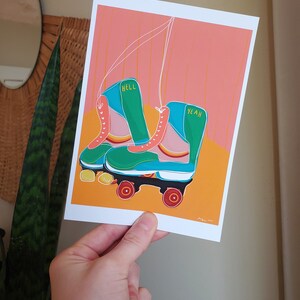 Puede incluir: Un par de patines de ruedas verdes y azules con ruedas blancas y detalles naranjas. Los patines tienen las palabras "Hell Yeah" escritas en ellos.