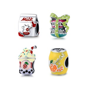 Puede incluir: Cuatro abalorios con pintura de esmalte y detalles plateados. Los abalorios tienen forma de cartón de leche con una vaca, una caja de regalo con un lazo, una taza de té de burbujas con una fresa y una lata de soda de naranja.