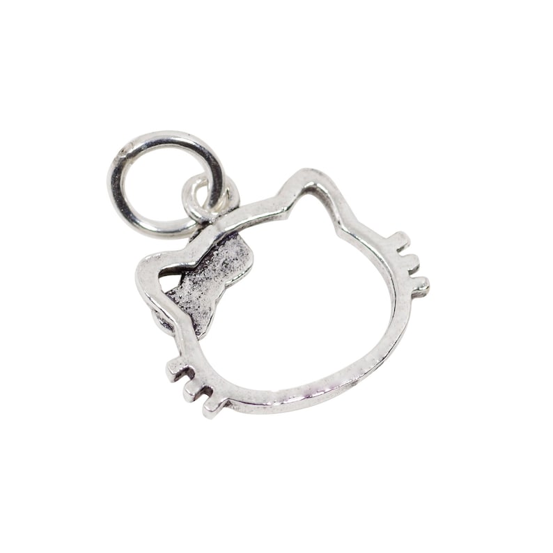 May include: A silver-colored charm in the shape of a cat's head with a bow. The charm has a loop at the top for attaching to a bracelet or necklace. The cat's face is outlined with small details for the eyes and whiskers.