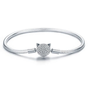 May include: A silver bracelet with a snake chain design. The focal point is a cat-shaped charm encrusted with small, sparkling crystals. The bracelet is a delicate piece of jewelry.