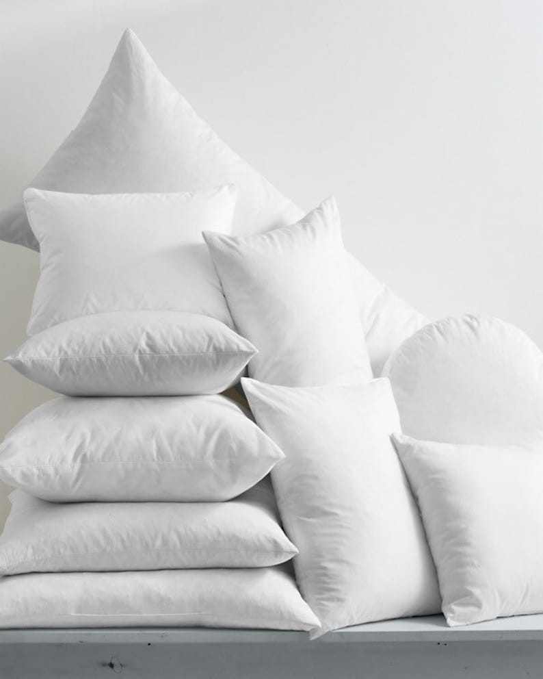 May include: A stack of white pillows of various sizes and shapes, arranged in a pyramid formation.