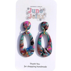 Peut inclure: Boucles d'oreilles pendantes avec des gouttes ovales au motif marbré rose, bleu sarcelle, bleu et noir avec des paillettes dorées. Les boucles sont fixées sur une carte blanche avec le texte Juno Jemz et Thank You for shopping handmade.