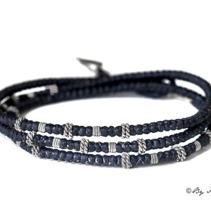 May include: A black braided cord bracelet with silver beads. The bracelet is wrapped three times around the wrist.