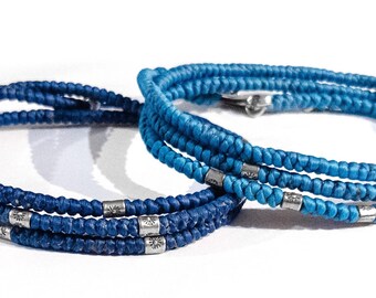 May include: Two braided bracelets with silver beads. The bracelet on the left is dark blue and the bracelet on the right is a lighter shade of blue.