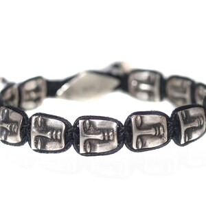 Könnte beinhalten: Ein schwarzes Armband mit silbernen Gesichtsanhängern. Die Gesichter sind stilisiert und haben ein minimalistisches Design.