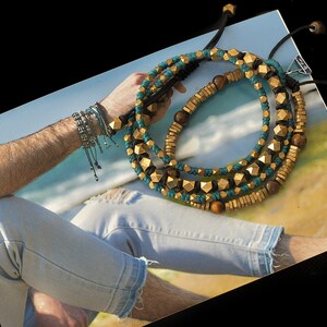 May include: A layered necklace with gold and turquoise beads. The necklace is made of metal and wood beads. The necklace is on a white surface.