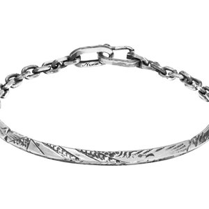 May include: A silver bracelet with a textured, patterned band and a chain link clasp. The bracelet is marked with the word "Neva".