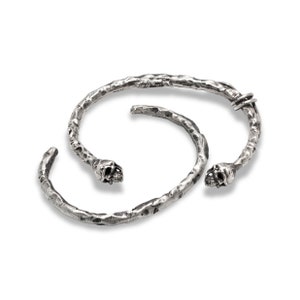 May include: Two silver skull-shaped bracelets with a textured finish. The bracelets are open and have a hinged clasp.