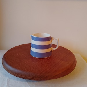 May include: A small, white ceramic creamer with blue and white stripes. The creamer is sitting on a wooden surface.