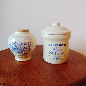 May include: Two ceramic jars with lids. The jar on the left is white with blue and brown details and says "Fortnum & Mason English Mustard". The jar on the right is white with blue details and says "Long Clawson Blue Stilton Stilton makers for over 100 years".