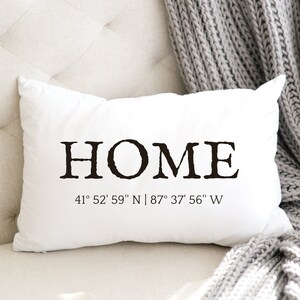 May include: White throw pillow with black text that reads "HOME" and the coordinates "41° 52' 59" N | 87° 37' 56" W".