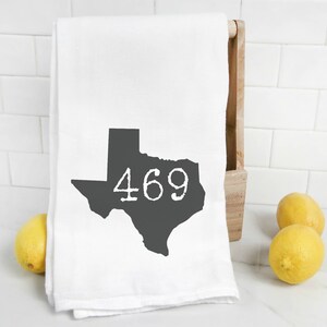 May include: White kitchen towel with a black outline of the state of Texas and the number 469 printed in white inside the state outline. Two yellow lemons are in the foreground.