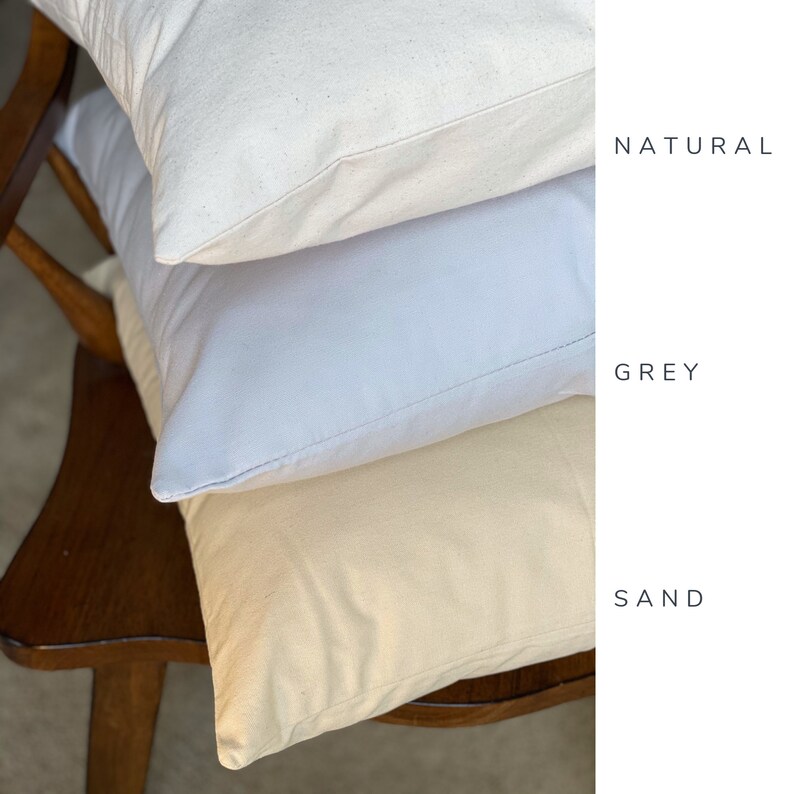 Pode incluir: Tr&ecirc;s capas de almofada em cores diferentes: natural, cinza e areia. As capas de almofada est&atilde;o empilhadas umas sobre as outras numa cadeira de madeira.