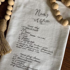 May include: A white kitchen towel with handwritten instructions for making a meatloaf. The instructions include ingredients like ground meat, onion, garlic, salt, pepper, bread crumbs, and eggs. The towel also includes instructions for making a meatloaf sauce.