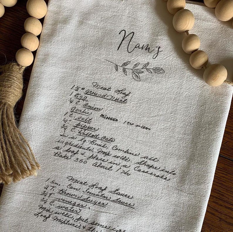 May include: A white kitchen towel with handwritten instructions for making a meatloaf. The instructions include ingredients like ground meat, onion, garlic, salt, pepper, bread crumbs, and eggs. The towel also includes instructions for making a meatloaf sauce.