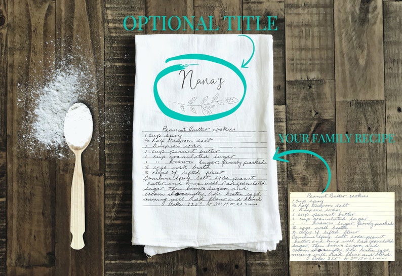 May include: A white tea towel with a handwritten peanut butter cookie recipe titled "Nana's". The recipe is written in black ink and includes ingredients like peanut butter, sugar, and eggs. The towel is on a wooden surface with a wooden spoon and a small pile of white powder.