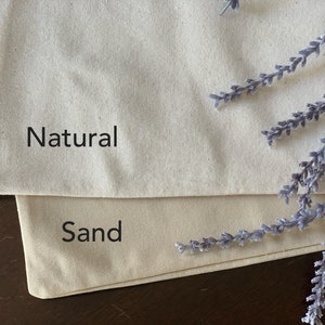 May include: Two pieces of fabric, one labeled "Natural" and the other labeled "Sand". The fabric is a natural off-white color.
