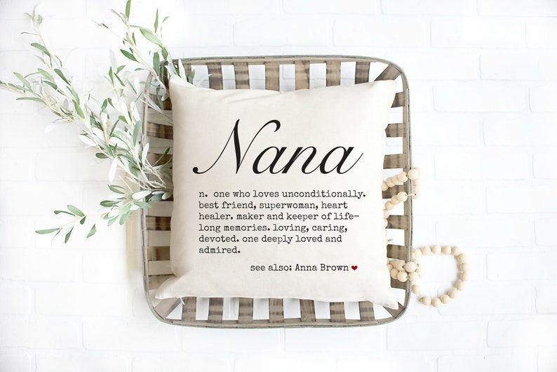 May include: A white throw pillow with the word "Nana" written in cursive script. The pillow has a definition of the word "Nana" that reads: "n. one who loves unconditionally, best friend, superwoman, heart healer, maker and keeper of life-long memories. loving, caring, devoted, one deeply loved and admired. see also: Anna Brown"