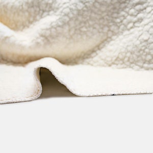 May include: A close-up of a white faux fur blanket with a soft, fluffy texture. The blanket is folded over, revealing the white fabric underneath.