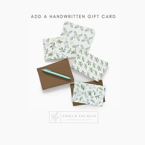 May include: An assortment of gift cards with floral and leaf patterns, a brown card, and a teal pen. The text "ADD A HANDWRITTEN GIFT CARD" is at the top. The bottom right corner has the text "EMMA & THE BEAN personalized gifts".