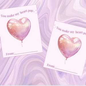 May include: Two pink cards featuring heart-shaped balloon illustrations. The cards have the text "You make my heart pop" and a line for "From:". The background is a light purple marble effect.