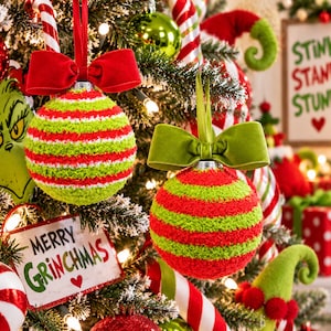 May include: Two round Christmas ornaments with fuzzy textures, one featuring horizontal lime green and white stripes with a red velvet bow, and the other with lime green and red stripes topped with a green velvet bow, hanging on a tree.