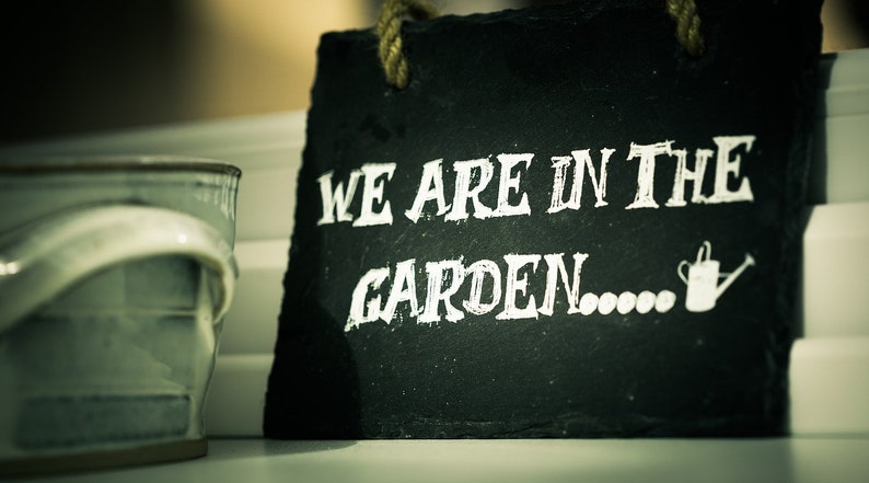 May include: Black chalkboard sign with white text that reads "We are in the garden..." with a small white watering can icon.