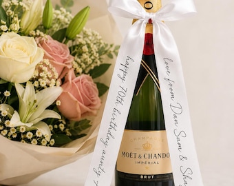 May include: A bottle of Moët & Chandon Impérial Brut champagne featuring a white satin ribbon tied around the neck. The ribbon is printed with the black text "happy 70th birthday aunty Alison" on one side and "love from Dan Sam & Shay xx" on the other.