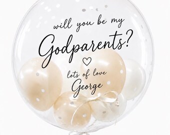 May include: A large clear balloon filled with smaller beige and white balloons. The text "will you be my Godparents?" is printed in black script, followed by a small heart and the text "lots of love George" with a white ribbon tied at the base.