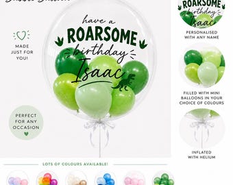 May include: A clear bubble balloon filled with smaller green balloons, featuring the black text "have a ROARSOME birthday Isaac" and a small dinosaur silhouette. The balloon is tied with a white ribbon and is inflated with helium.