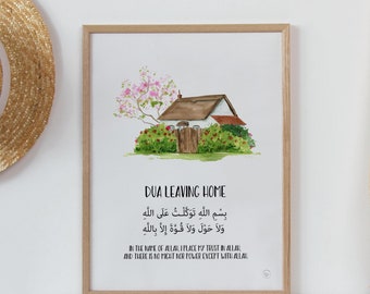 May include: A framed watercolour print featuring the text "DUA LEAVING HOME" and Arabic script. The artwork shows a small house with a thatched roof, surrounded by greenery and pink flowering trees. The print includes the artist's studio name and website.