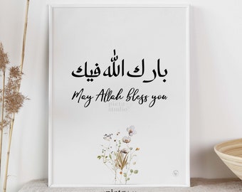 May include: A white framed print with black calligraphy that reads "May Allah bless you" in English and Arabic. The print features a watercolor illustration of a bouquet of white and brown flowers.
