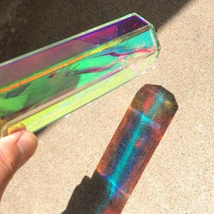 Puede incluir: Un prisma transparente con colores arcoíris iridiscentes proyecta un reflejo colorido sobre una superficie gris claro.