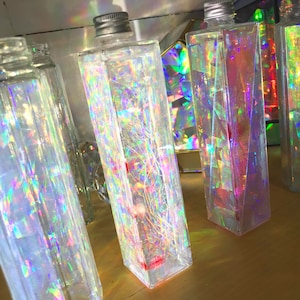 May include: Four clear glass bottles filled with iridescent glitter and a swirling pattern. The bottles are rectangular and have a silver lid.