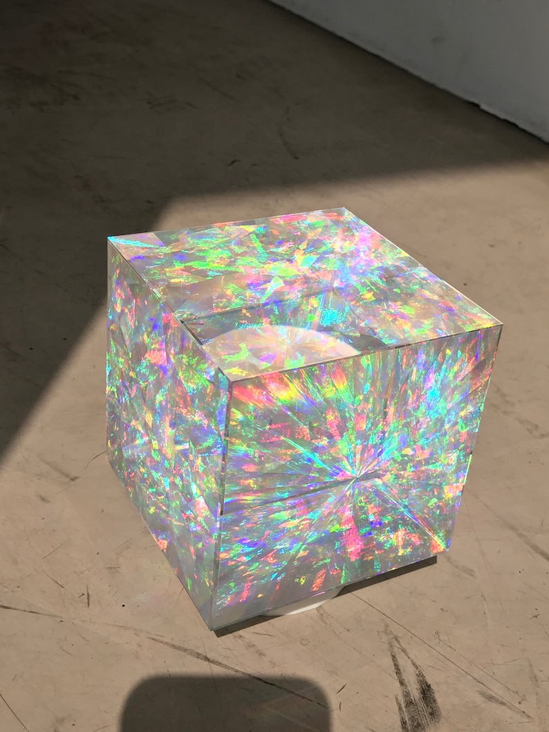 May include: A clear cube with iridescent rainbow colors. The cube is made of glass and has a reflective surface.