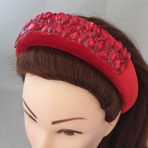 Op de afbeelding: Een rode haarband met een fluweelachtige textuur, versierd met een rij grote, druppelvormige rode strass-steentjes. Het haaraccessoire wordt getoond op een mannequinhoofd met bruin haar.