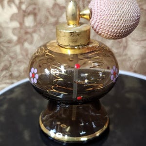 May include: A vintage perfume bottle with a brown glass body, gold accents, and a pink atomizer. The bottle is decorated with floral designs and red and purple accents. A classic collectible.